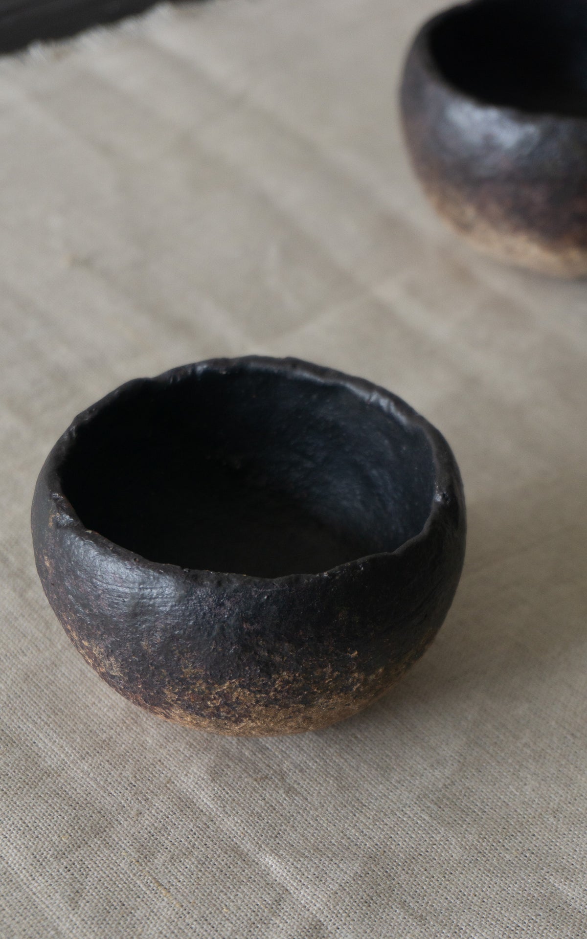 Black ceramic bowl shaped cup on a textured beige surface