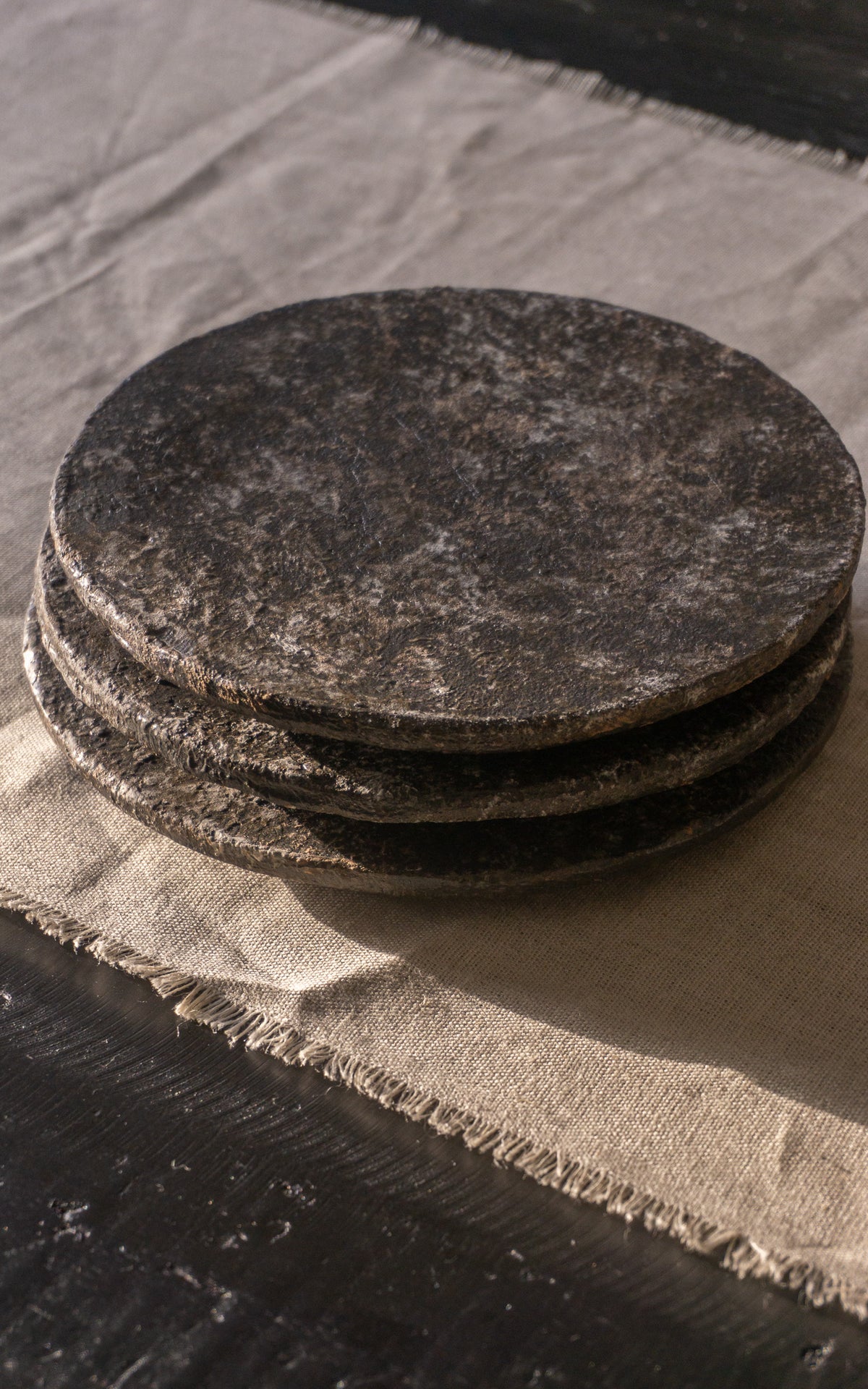 Stack of dark gray ceramic flat plates on a textured surface