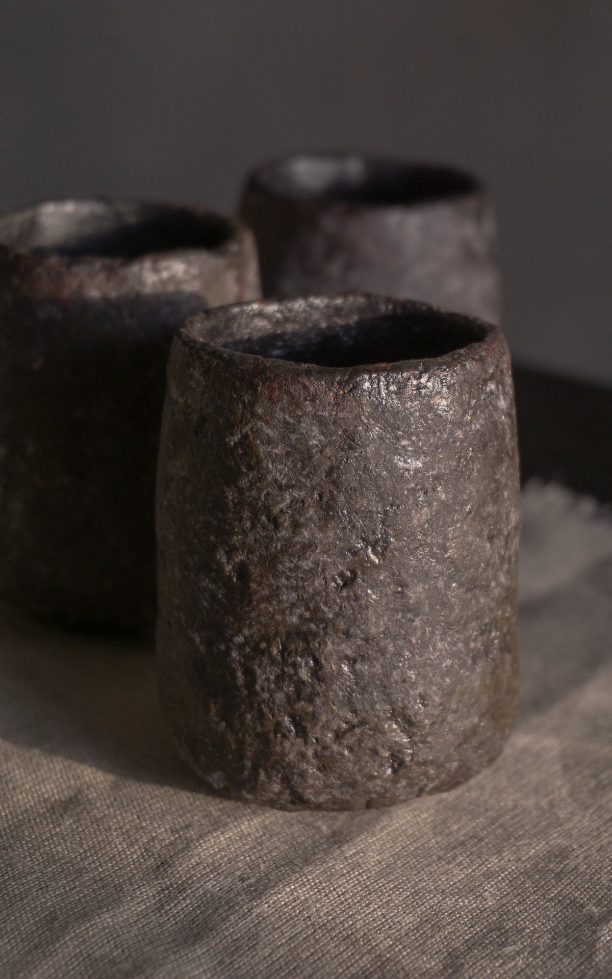 Three dark ceramic cups on a textured surface with a neutral background
