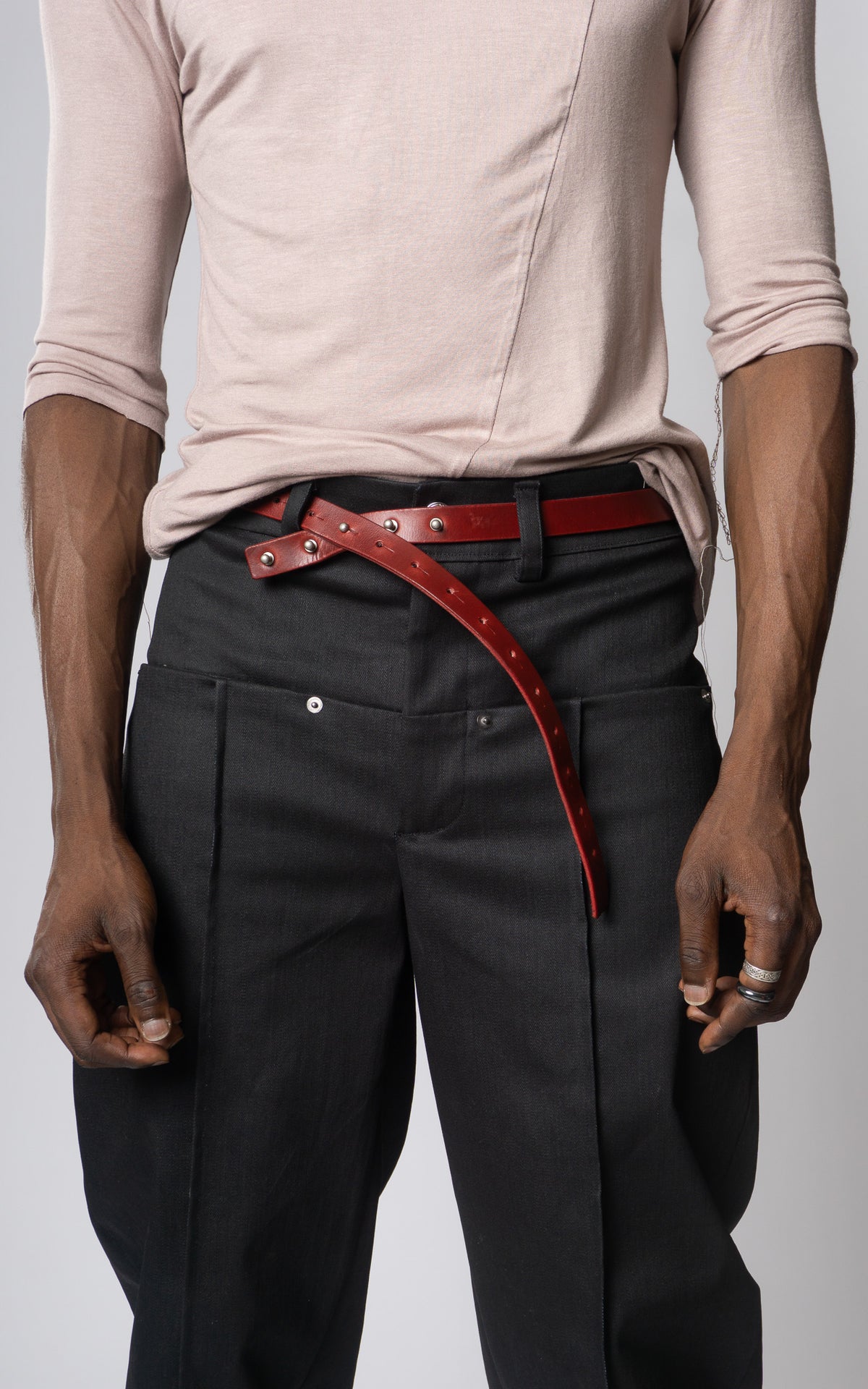 Person wearing black pants with a red stud belt on a plain background
