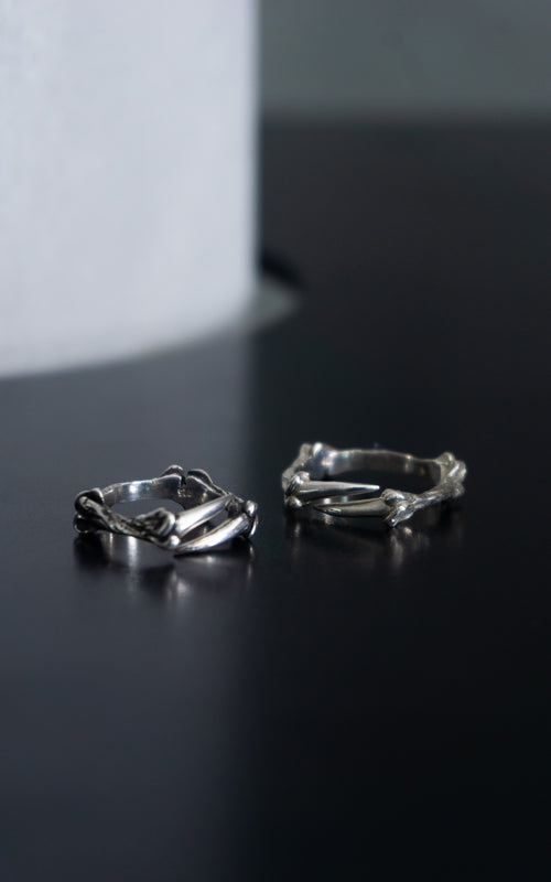 Two silver rings with organic, twisted, bone-like shapes resting on a dark reflective surface.