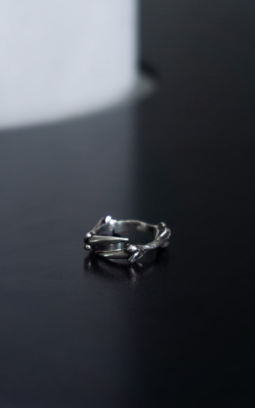A silver ring with a twisted, organic branch-like design, resting on a dark reflective surface.